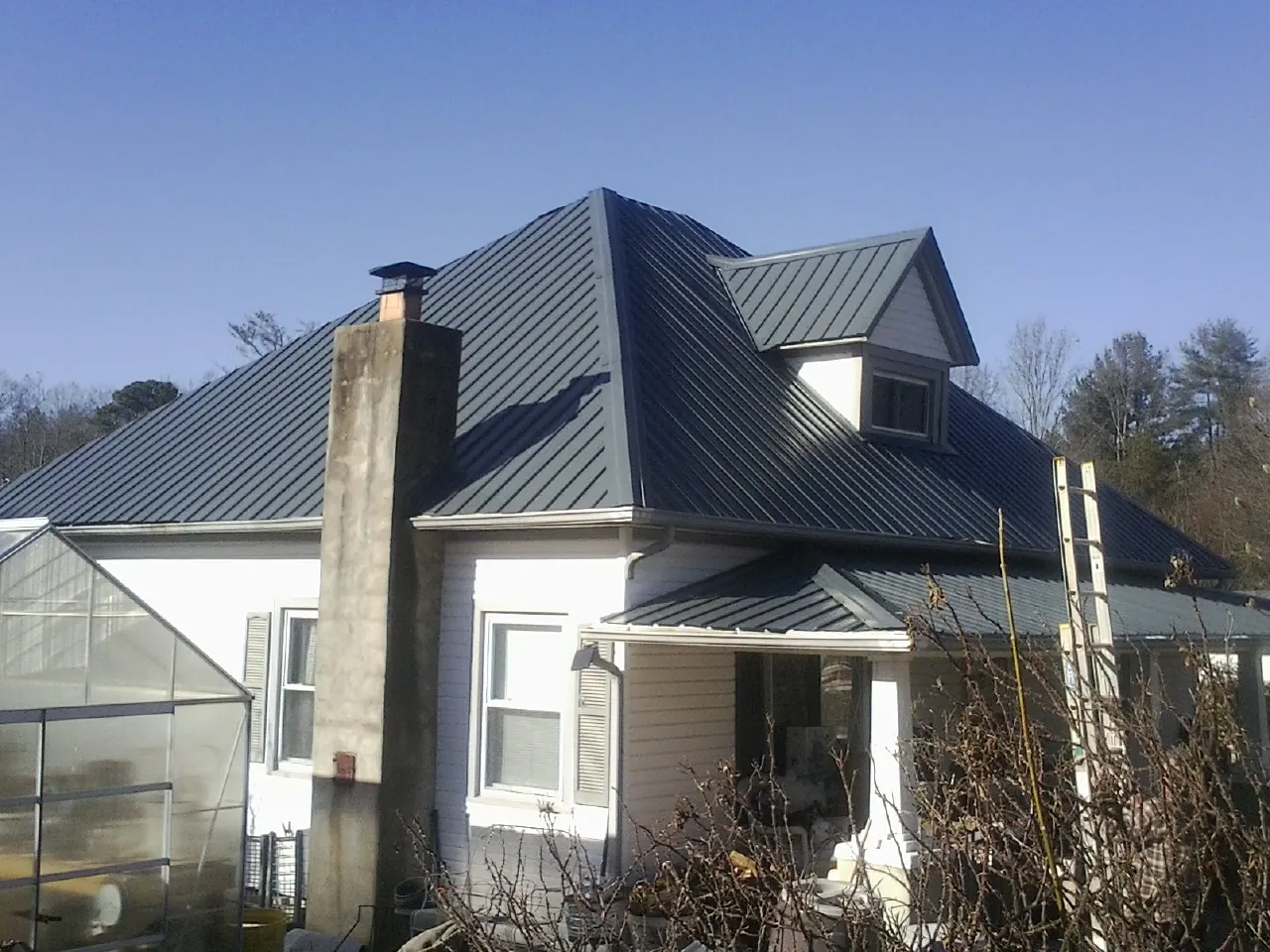 Dark blue standing seam metal roof on a white farmhouse with dormer — Slate & Tile Roof Repair by Roofing Brothers in New Stanton