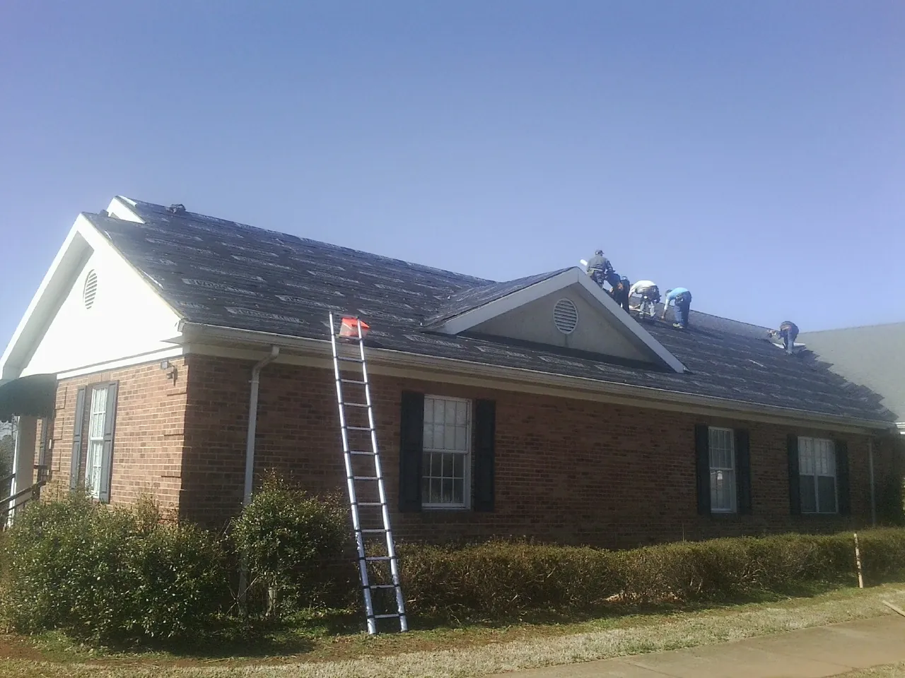 Crew tearing shingles off a brick ranch roof with a ladder set — Metal Roof Repair work by our crew in New Stanton