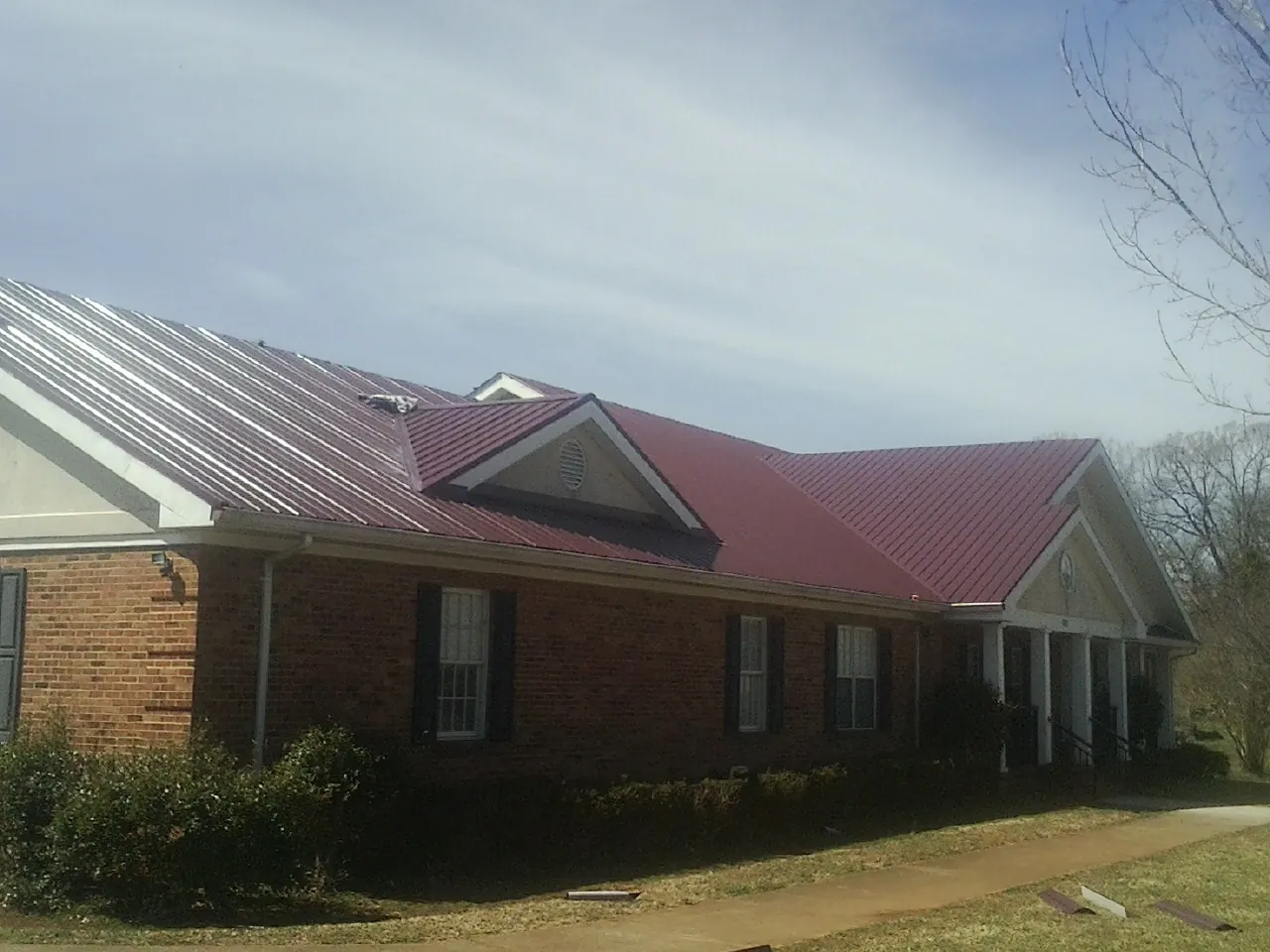 Red metal roof with gabled entries on a long brick building, from a Hail Damage Roof Repair job in New Stanton