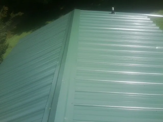 New green metal panels meeting at the ridge of a roof — Flat Roof Repair work by our crew in New Stanton