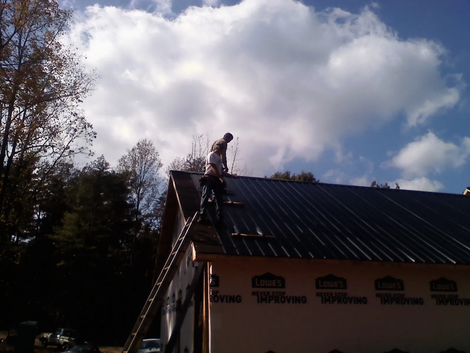 Roofer fastening dark metal panels high against a cloudy sky, from a Roof Inspection job in New Stanton