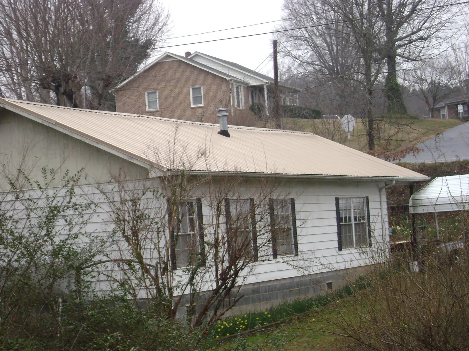 Tan metal roof on a white sided house set into a hillside — Commercial Roofing by Roofing Brothers in New Stanton
