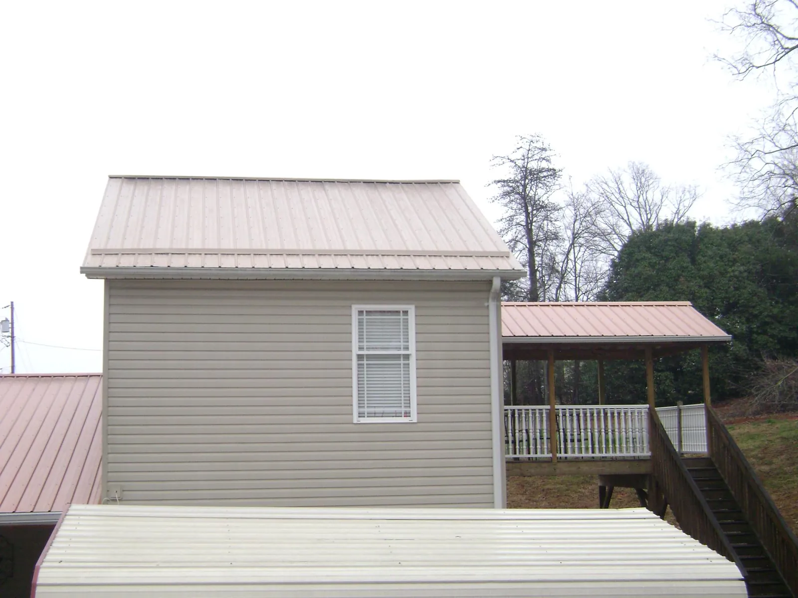 Tan metal roofs on a two story addition and attached porch, from a Roof Replacement job in New Stanton